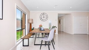 A modern dining area with a wooden table, chairs, and a large wall clock. - Point Cook Serenity Stay (Point Cook)
