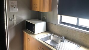 Una cocina compacta con microondas, un lavamanos, armarios de madera y una ventana con persiana.