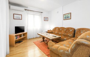 A living room with a sofa, a TV, a wooden shelf with books, and a window with curtains.