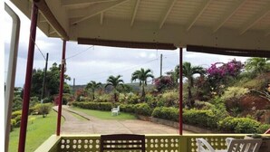 A covered outdoor area with a bench and a table, surrounded by lush greenery and palm trees.