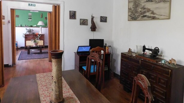 A room with a wooden dining table, a laptop on a desk, a sewing machine, and a traditional Chinese painting on the wall. - Wind Hostel (Valparaíso)