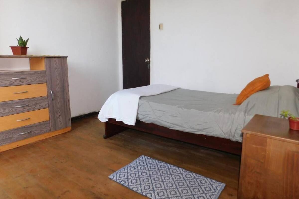 Una camera da letto con un letto, una cassettiera, una porta e un piccolo tappeto.