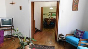 A living room with a television, a coffee table with a plant, a blue sofa, and a wooden floor. - Wind Hostel (Valparaíso)