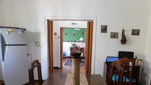 A dining area with a wooden table, chairs, a decorative vase, a refrigerator, a laptop, and a television. - Wind Hostel (Valparaíso)