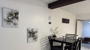 Ein Essbereich mit einem dunklen Holztisch und Stühlen, einer Vase mit weißen Blumen und zwei abstrakten Bildern an der Wand.