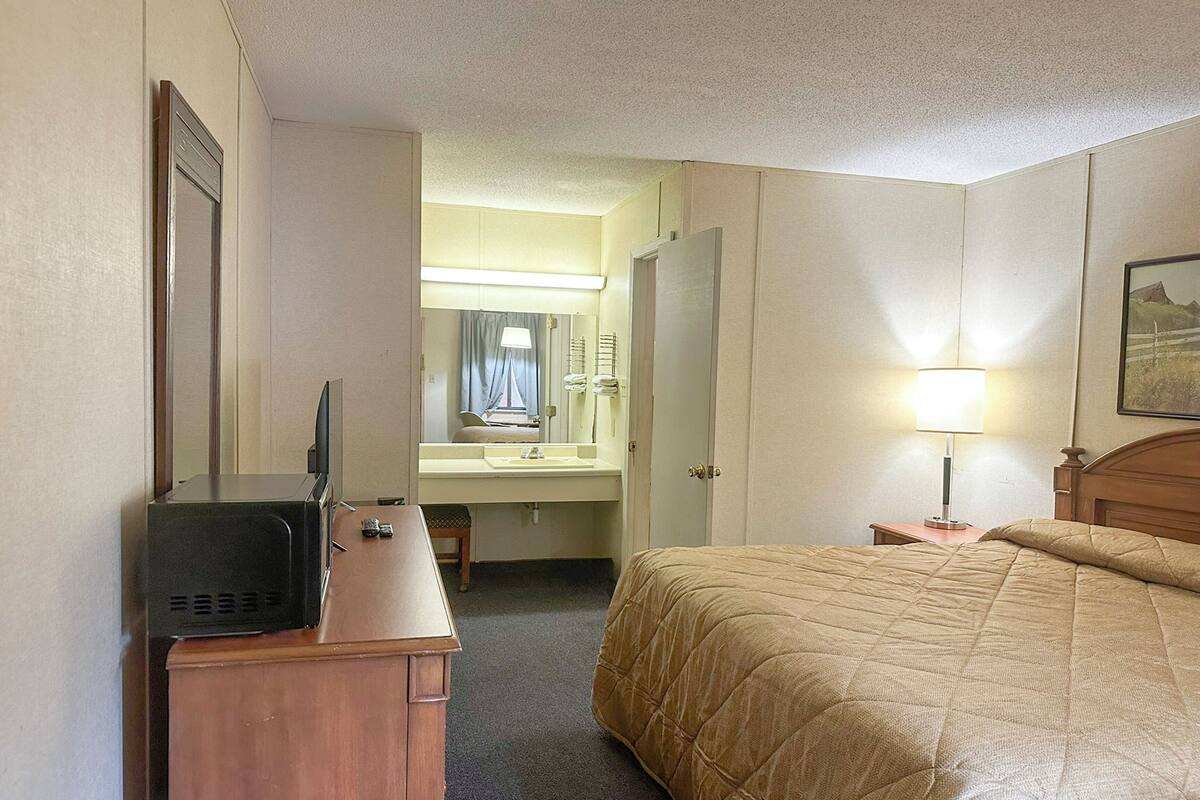 A hotel room with a bed, a desk with a television, a bathroom with a sink and mirror, and a nightstand with a lamp.