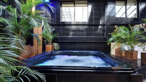 A hot tub surrounded by potted plants in a modern indoor setting with dark tiled walls and windows. - Park Lleras 11br Pool Jacuzzi (Medellín)