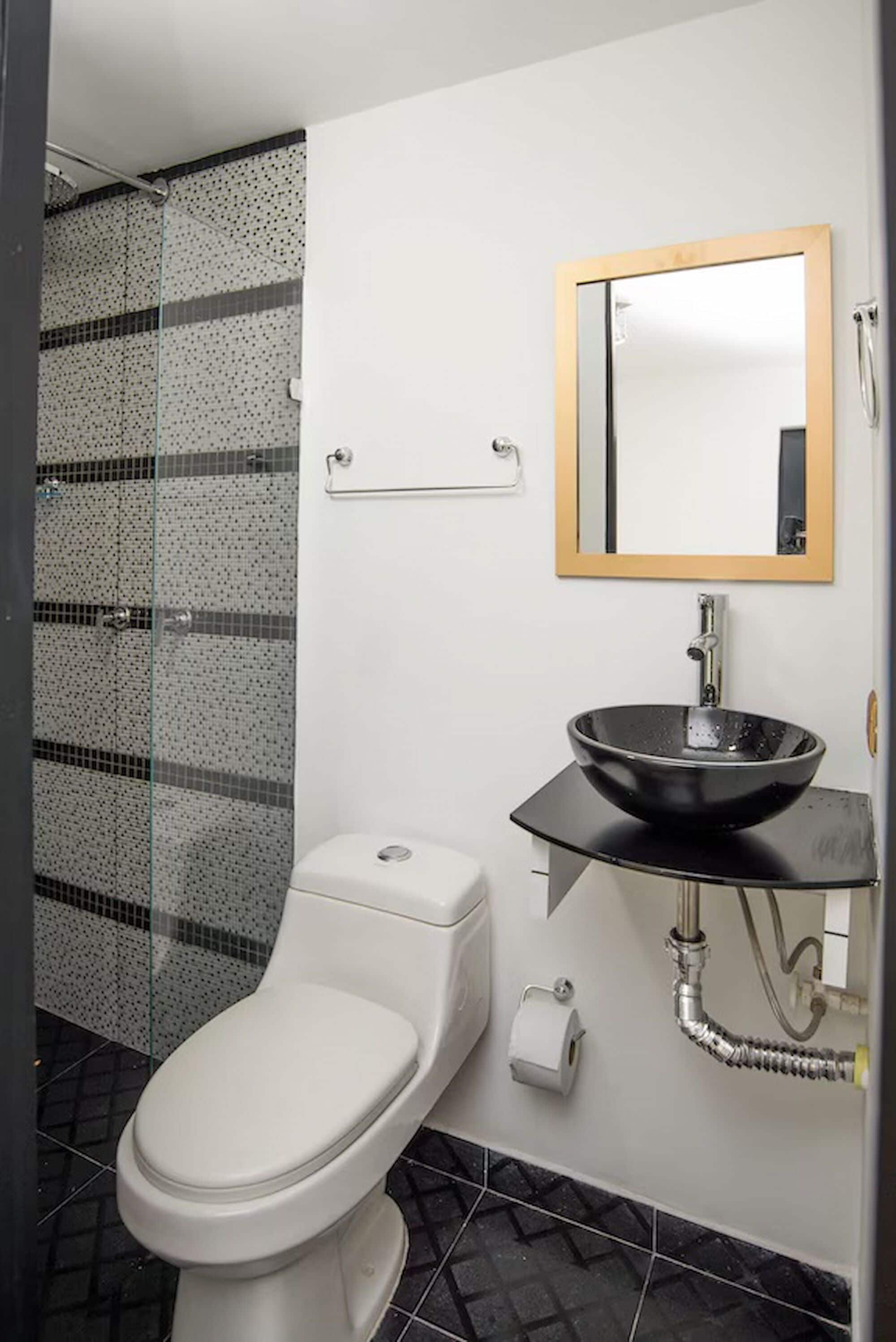A bathroom with a white toilet, a black vessel sink, a glass shower enclosure, and a mirror with a wooden frame.