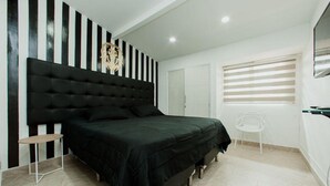 A bedroom with a black upholstered headboard, a bed with a dark green bedspread, a small round table, and a white chair. - Park Lleras 11br Pool Jacuzzi (Medellín)