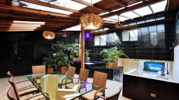A modern indoor dining area with a glass table, wicker chairs, and potted plants. - Park Lleras 11br Pool Jacuzzi (Medellín)