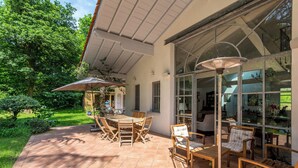 Eine Terrasse im Freien mit Tisch und Stühlen, umgeben von Glaswänden und einem Garten.