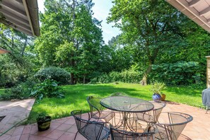 A patio with a round table and chairs, surrounded by lush greenery and trees. - Villa Bichipau Park - Welkeys (Bidart)