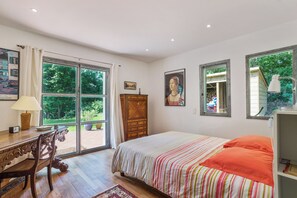 A bedroom with a large bed, a wooden desk, a chair, a dresser, and a window with a view of greenery. - Villa Bichipau Park - Welkeys (Bidart)