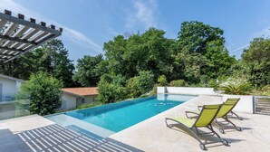Ein Swimmingpool mit klarem, blauem Wasser, umgeben von einer Terrasse mit zwei Liegestühlen und einer Pergola.