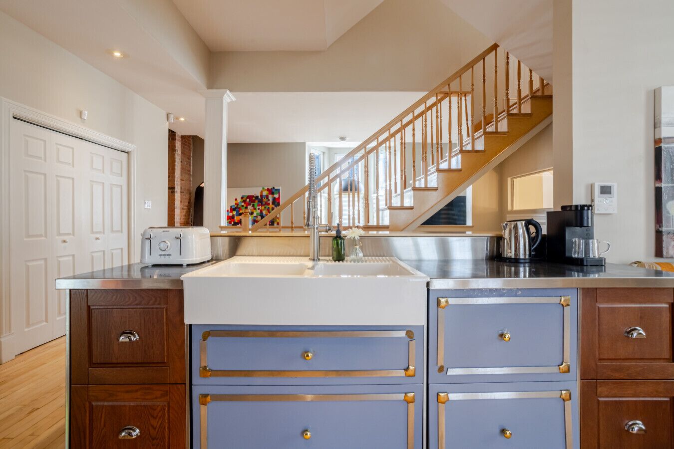 A kitchen with a central island, wooden cabinets, a stainless steel range hood, and a staircase leading to another level.
