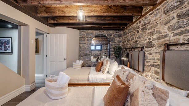 Ein gemütliches Schlafzimmer mit einer Steinwand, einer Holzbalkendecke, einem Bett mit weißer Bettwäsche und einer Pendelleuchte.