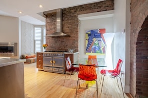 A modern kitchen with a brick wall, a stainless steel stove, and a glass dining table with red chairs.