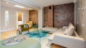 Ein modernes Wohnzimmer mit einer Ziegelwand, einem Glastisch, einer Couch und einem grünen Sessel.