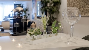A dining table with a white centerpiece featuring glass vases with green plants and a clear wine glass.