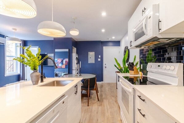 A modern kitchen with white appliances, a dining area with a round table, and blue walls.