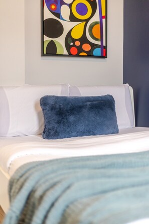 Un letto con un cuscino blu e una coperta bianca.