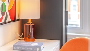 Habitación de hotel con una lámpara moderna, un cuadro abstracto colorido y vistas al exterior.