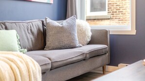 Un sofá gris con varios cojines en una habitación con ventana y pared de ladrillo.