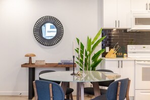 A modern kitchen with white cabinets, a microwave, and a stove. There's a round table with chairs and a potted plant.