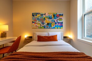 A hotel room with a bed, a desk, a chair, and a colorful abstract painting on the wall. - Beautiful 3BR in Plateau Mont-Royal (Montréal)