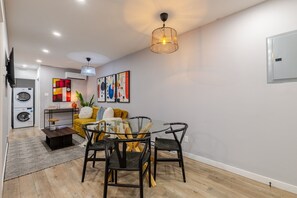 Un salon moderne comprenant un coin repas, un lave-linge et des œuvres d’art abstrait accrochées au mur.