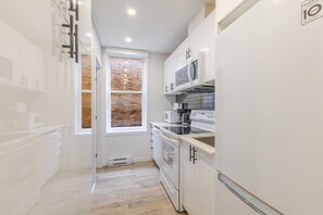 A modern kitchen with white cabinetry, a brick-patterned window, and a stainless steel refrigerator. - Beautiful 3BR in Plateau Mont-Royal (Montréal)