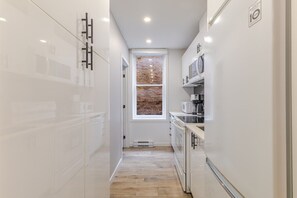 A narrow kitchen with white cabinetry, a brick wall through a window, and a microwave on the countertop. - Beautiful 3BR in Plateau Mont-Royal (Montréal)