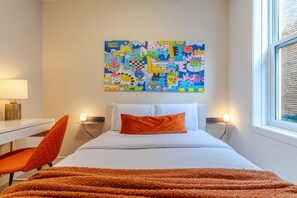 A hotel room with a bed, a desk, a chair, a colorful abstract painting on the wall, and a window. - Beautiful 3BR in Plateau Mont-Royal (Montréal)