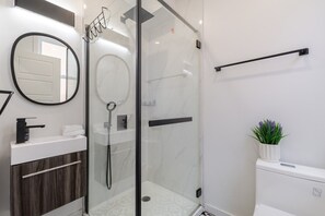 Une salle de bain moderne avec une douche en verre, un miroir rond, un lavabo blanc et une plante en pot.