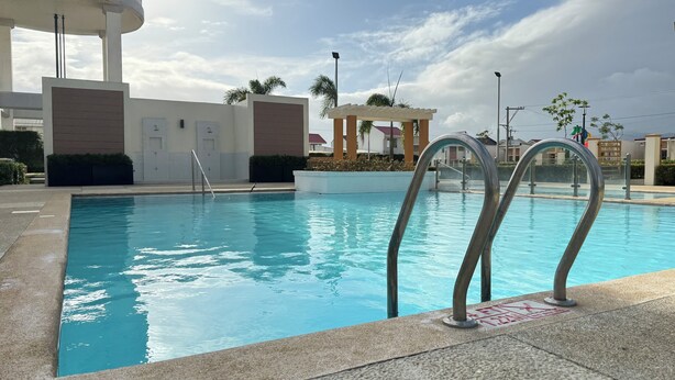 Ein Schwimmbecken mit Metallgeländern, ein überdachter Bereich mit Palmen und ein Gebäude mit modernem Design im Hintergrund.