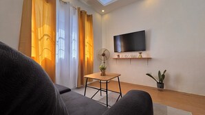 Ein modernes Wohnzimmer mit einem an der Wand befestigten Flachbildfernseher, einem kleinen Holztisch mit Pflanze und einem Sofa.