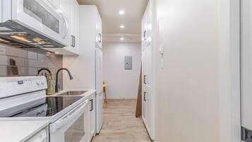 A narrow kitchen with white cabinets, a built-in oven, and a microwave.