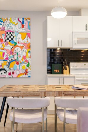 Une cuisine moderne avec des meubles blancs, une table à manger en bois et un tableau abstrait aux couleurs vives accroché au mur.