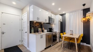 A compact kitchen with white cabinets, a stove, and a dining area with yellow chairs. - Elegant Living: 3-Bedroom in Plateau MTL (Montréal)