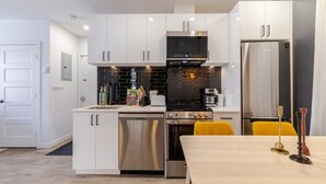 A modern kitchen with white cabinets, a black microwave, a stainless steel stove, and a refrigerator. - Elegant Living: 3-Bedroom in Plateau MTL (Montréal)