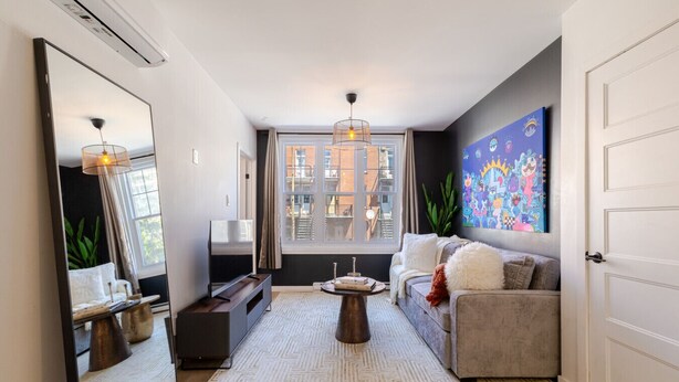 A modern living room with a sofa, a coffee table, a TV, and a large window. - Elegant Living: 3-Bedroom in Plateau MTL (Montréal)