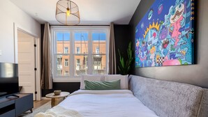 A bedroom with a bed, a TV, a painting, and a window with a view of buildings. - Elegant Living: 3-Bedroom in Plateau MTL (Montréal)