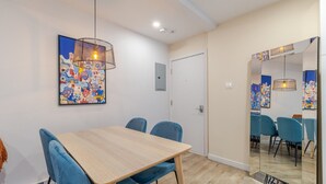 A dining area with a wooden table and blue chairs, a colorful abstract painting on the wall, and a door leading to another room. - Stunning 3BR in Plateau Mont-Royal (Montréal)