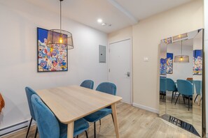 A dining area with a wooden table and blue chairs, a colorful abstract painting on the wall, and a door leading to another room. - Stunning 3BR in Plateau Mont-Royal (Montréal)