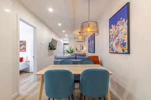 A modern dining area with a wooden table and teal chairs, a hanging light fixture, and colorful artwork on the walls.