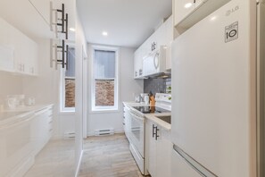 A modern kitchen with white cabinetry, an LG refrigerator, and a window with a brick wall view.