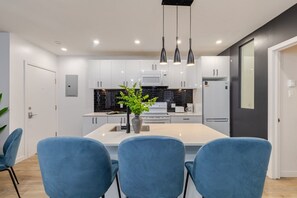 Cocina moderna con armarios blancos, una isla central y sillas azules.