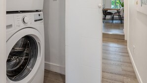 Une buanderie équipée de deux machines à laver superposées et d’une porte donnant sur un coin repas.