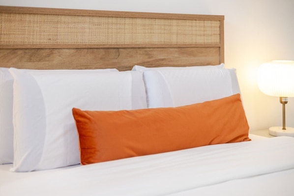 A bed with white and orange pillows, a wooden headboard, and a bedside lamp.