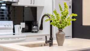 A modern kitchen with white cabinetry, a black faucet, and a potted plant on the island. - Vibrant 4BR/2BA Retreat in the Plateau (Montréal)